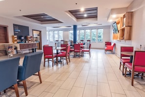 A modern dining area with red and blue chairs, a coffee station, and large windows offering natural light.