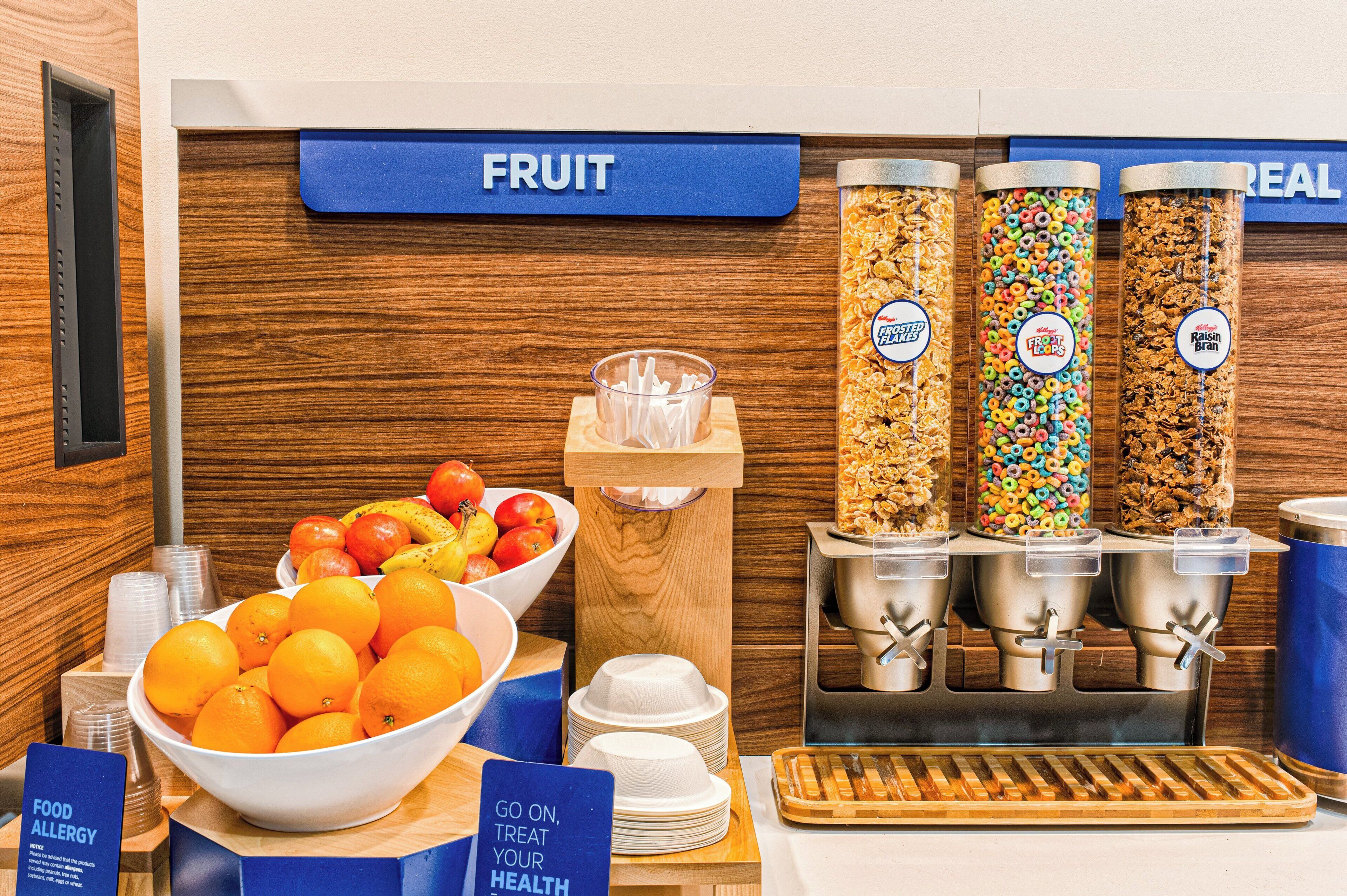 Un buffet de petit-déjeuner comprenant un assortiment de fruits, différentes sortes de céréales et un panneau invitant à prendre soin de sa santé.