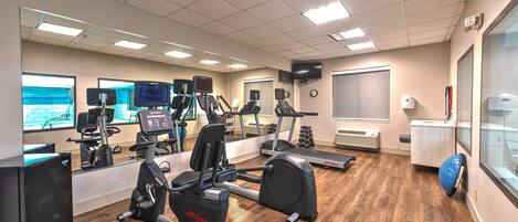 A gym with cardio equipment, mirrors, and a large window.