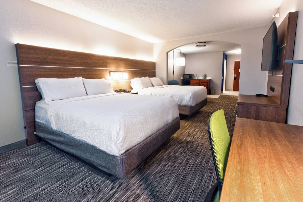 A hotel room with two beds, a desk, a chair, a TV, and a mirror.