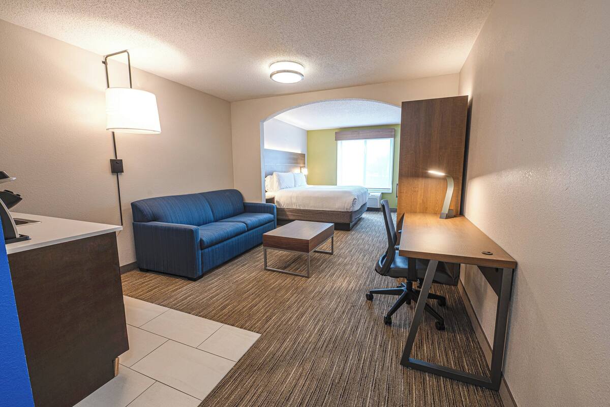 A hotel room with a bed, a blue sofa, a desk, and a lamp.