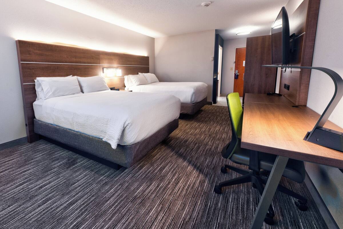 A hotel room with two beds, a desk, a chair, and a TV.