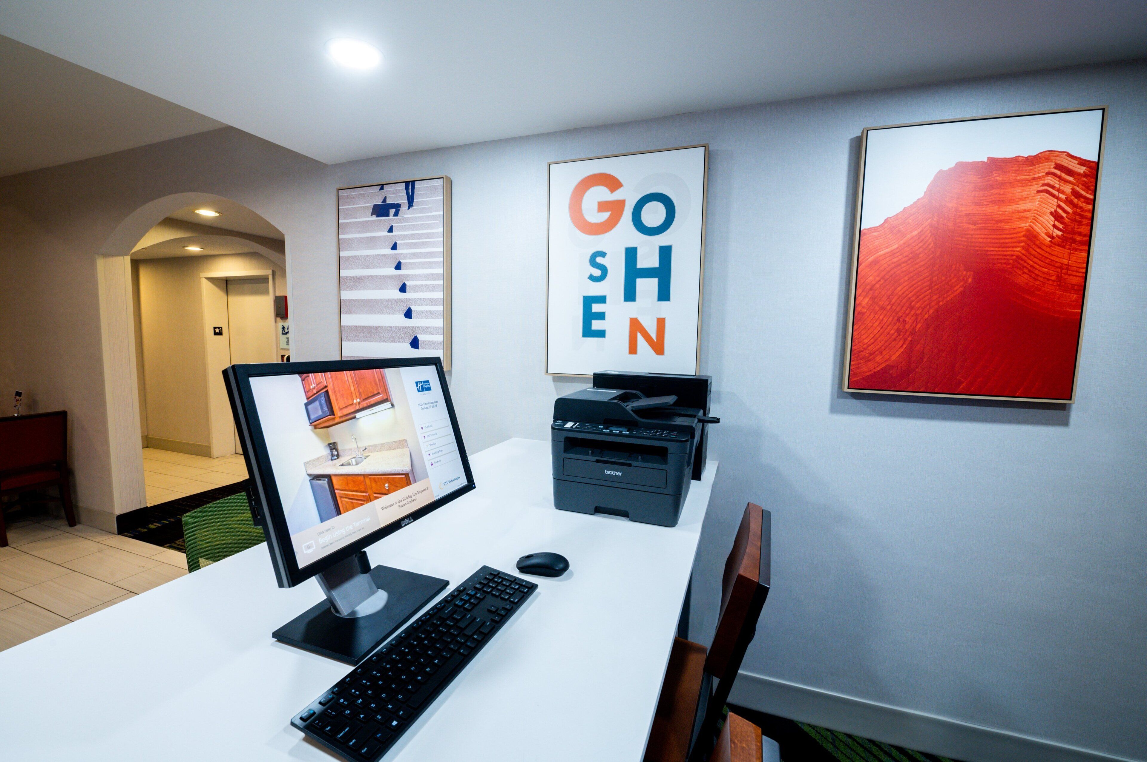 A modern office space with a desktop computer, a printer, and framed artwork on the wall.