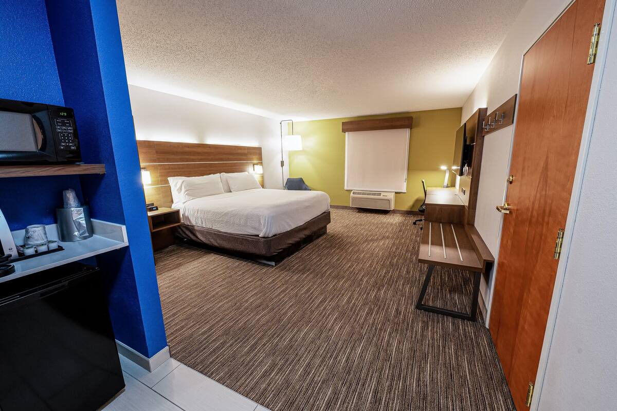 A hotel room with a bed, bedside tables, a desk with a microwave, a lamp, and a wardrobe.