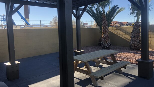 A covered outdoor area with picnic tables, palm trees, and a view of a construction site in the background.