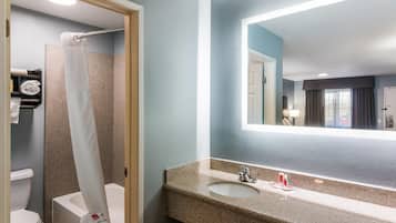 A bathroom with a shower, toilet, sink, and a mirror.