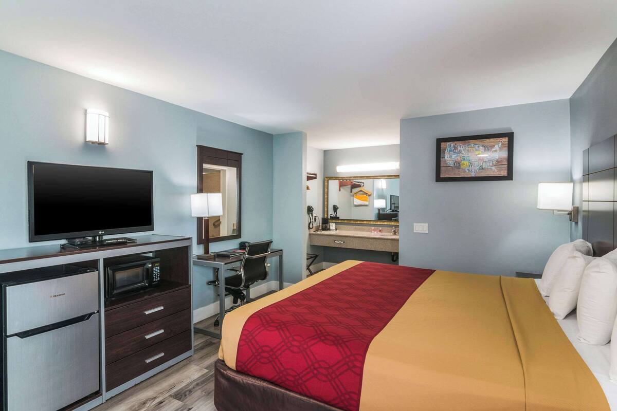 Ein Hotelzimmer mit einem Bett, einem Schreibtisch mit Computer, einem Fernseher, einer Mikrowelle und einem Kühlschrank.