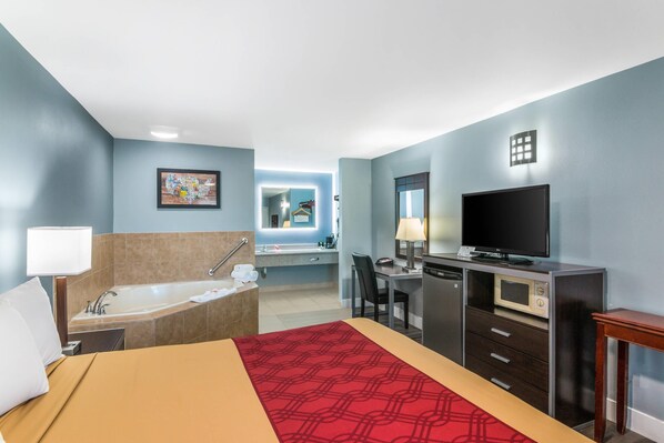 Una habitación de hotel con cama, escritorio, televisión, microondas y baño con bañera y lavamanos.