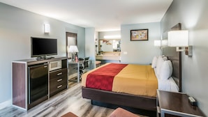 Habitación de hotel con cama, escritorio con computadora, televisión, microondas y baño con espejo y lavamanos.
