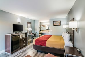 A hotel room with a bed, a desk with a computer, a television, a microwave, and a bathroom with a mirror and sink.