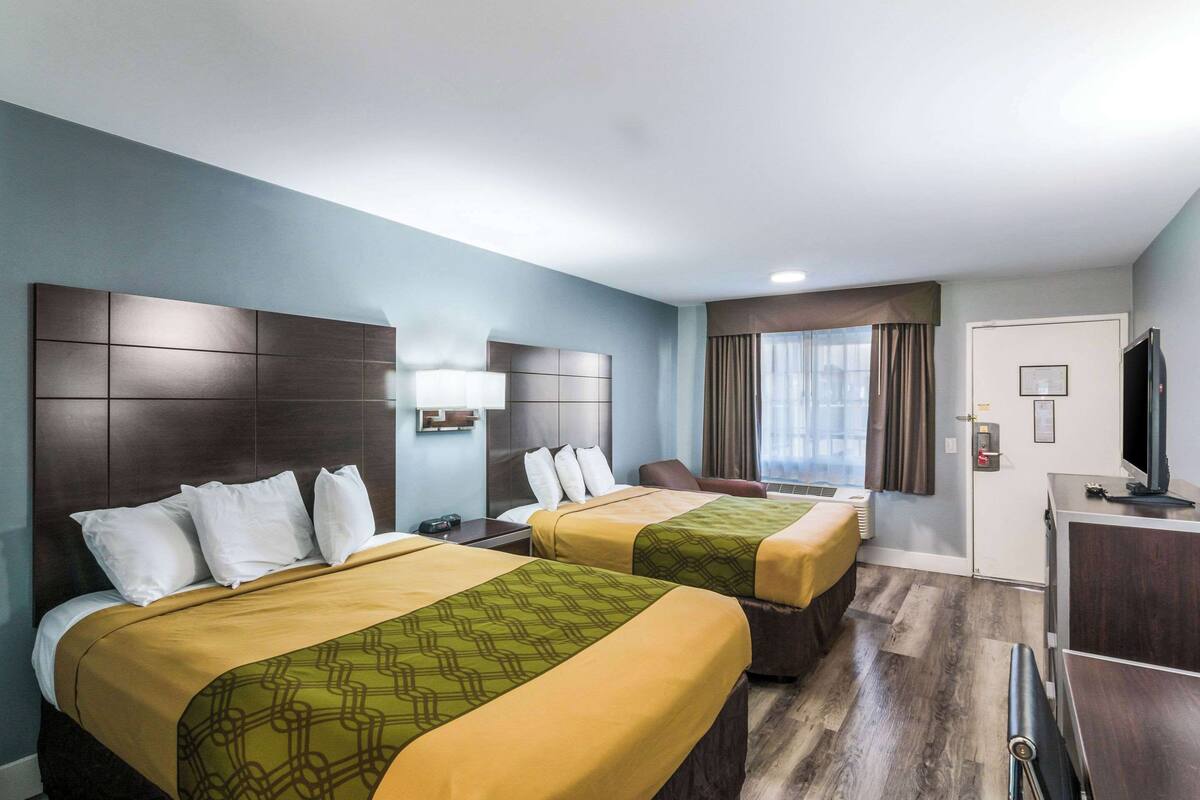 A hotel room with two beds, a desk, a TV, and a window with curtains.