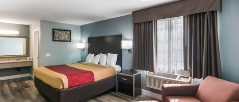 A hotel room with a bed, bedside table, lamp, chair, and a large window with curtains.