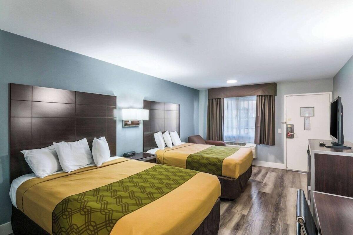 A hotel room with two beds, a desk, a TV, and a window with curtains.