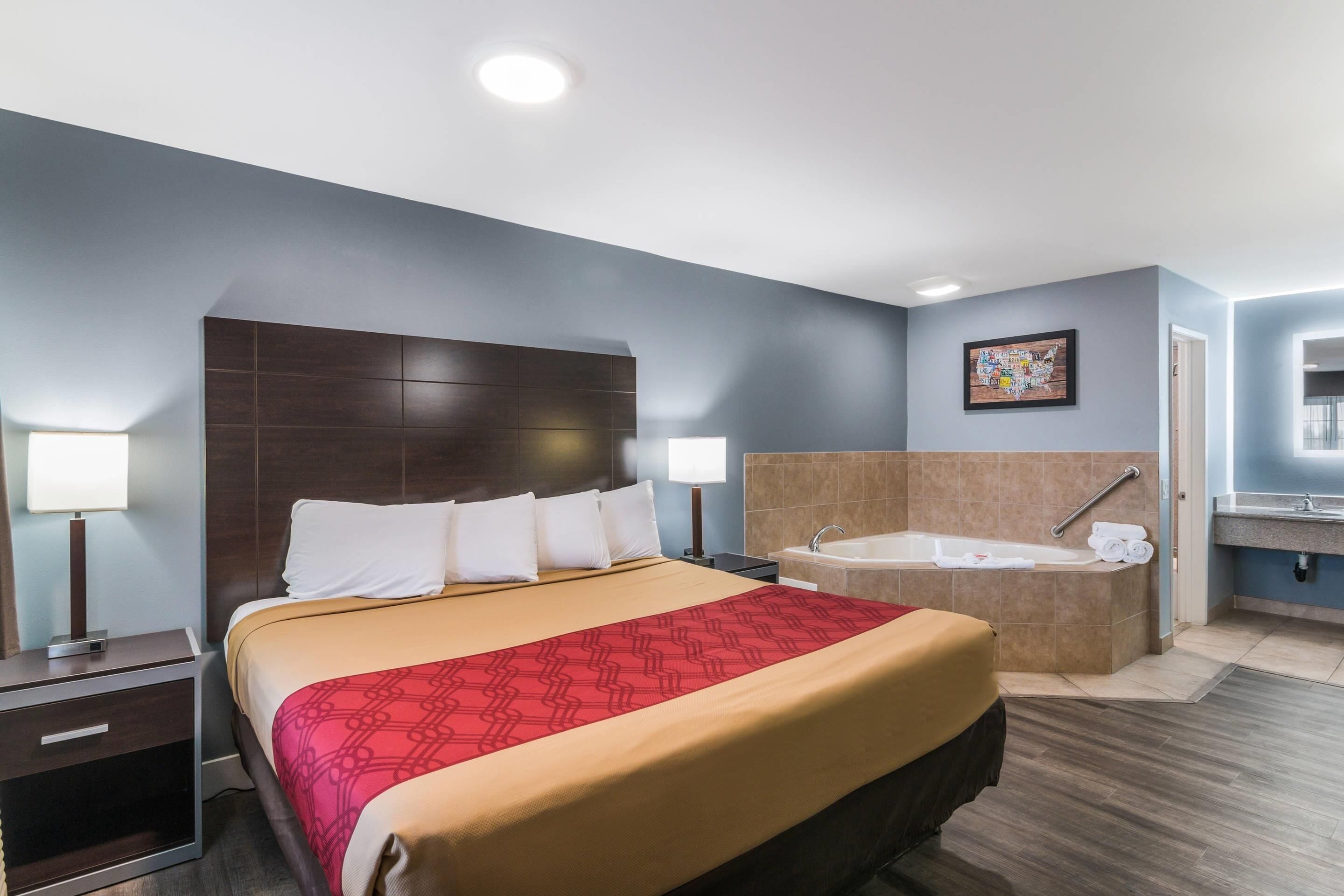 A hotel room with a large bed, a separate bathroom with a bathtub, and a small desk with a lamp.