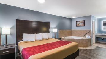 A hotel room with a large bed, a separate bathroom with a bathtub, and a small desk with a lamp.