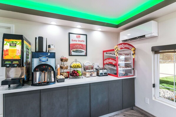 A self-service breakfast bar with a coffee machine, a juice dispenser, and a display case with pastries. - Econo Lodge Hesperia - Victorville I-15 (Hesperia)