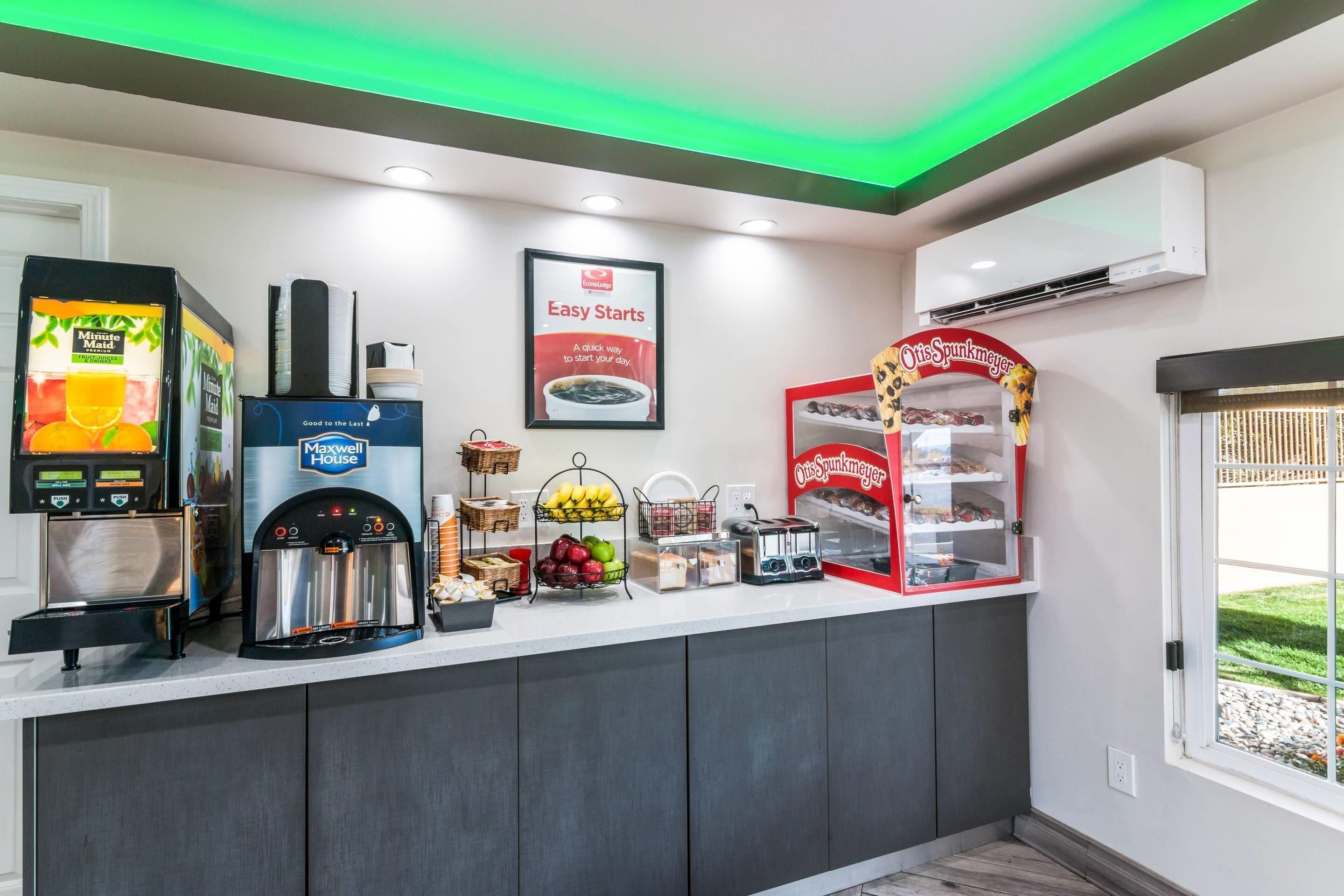 Un espace où l’on peut se servir soi-même pour le petit-déjeuner, comprenant une machine à café, un distributeur de jus et un grille-pain.