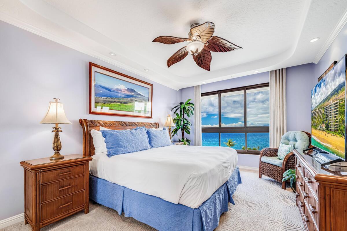 A bedroom with a bed, nightstands, a ceiling fan, a large window with a view, and a television.