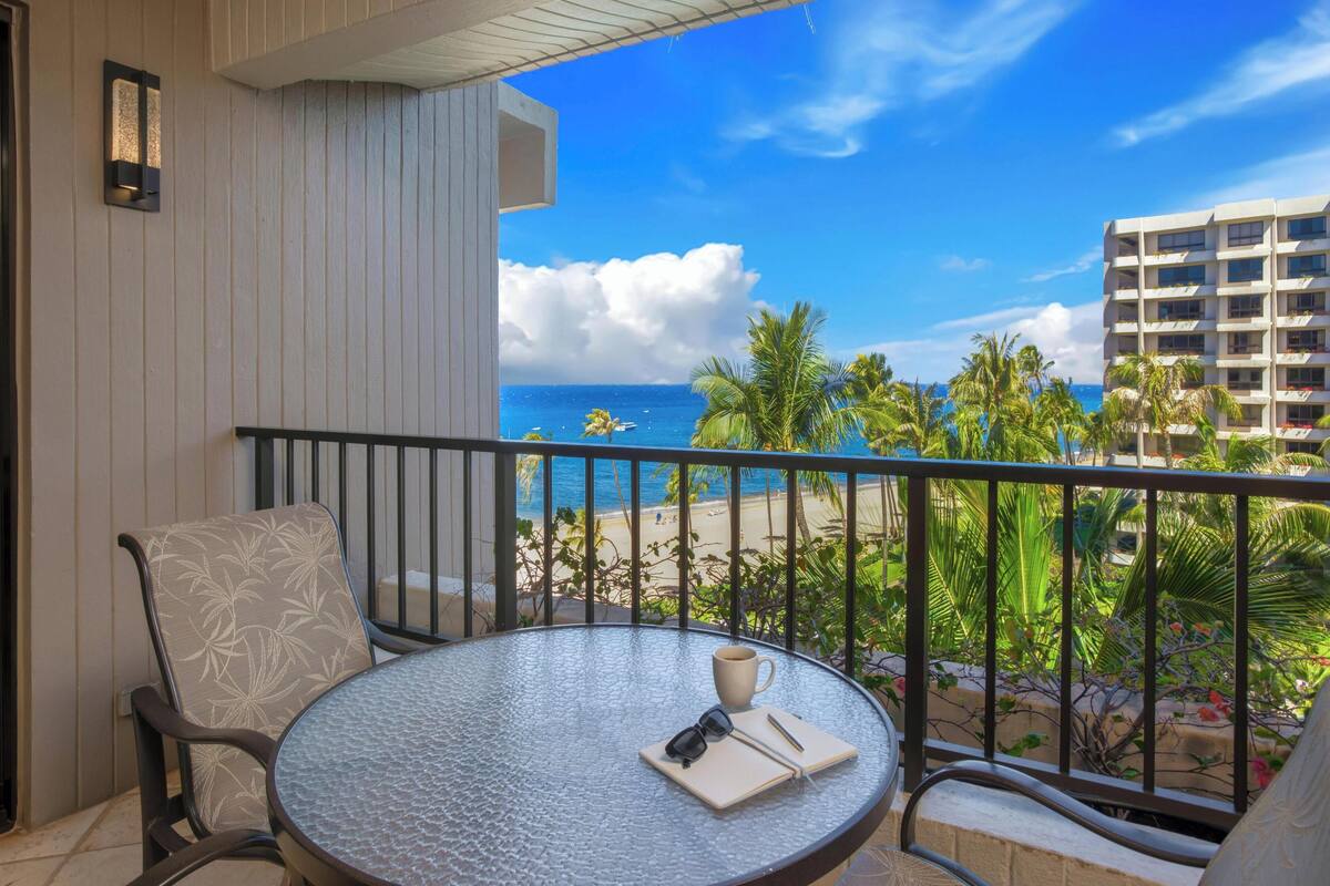A balcony with a round table, chairs, and a view of the beach and ocean.