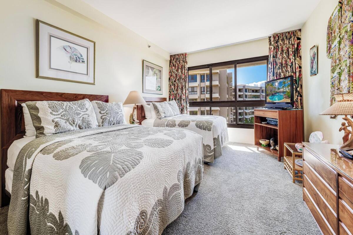 A hotel room with two beds, a TV, a desk, and a view of the city.