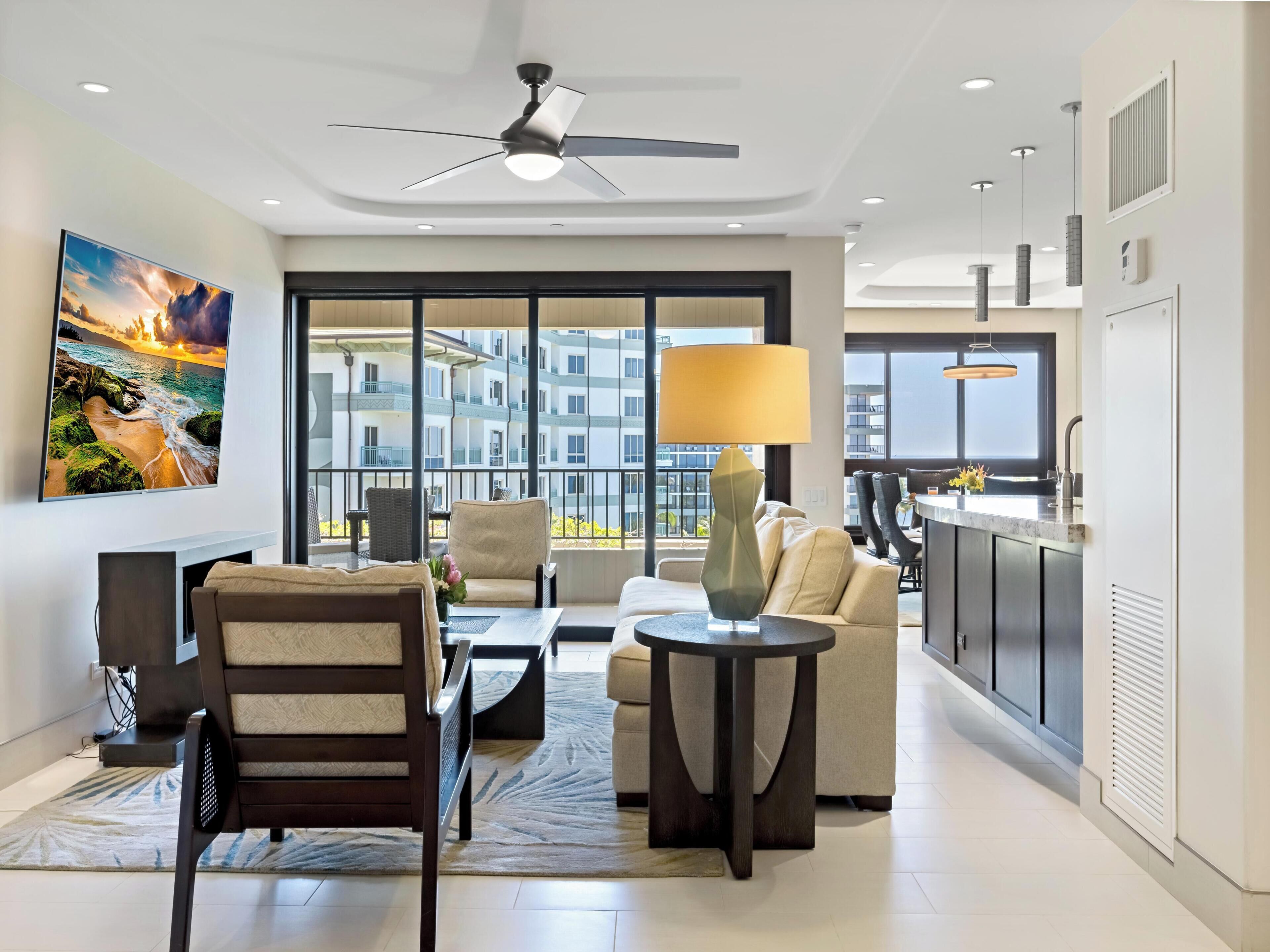A modern living room with a sofa, armchair, and coffee table, a ceiling fan, and a large window with a city view.