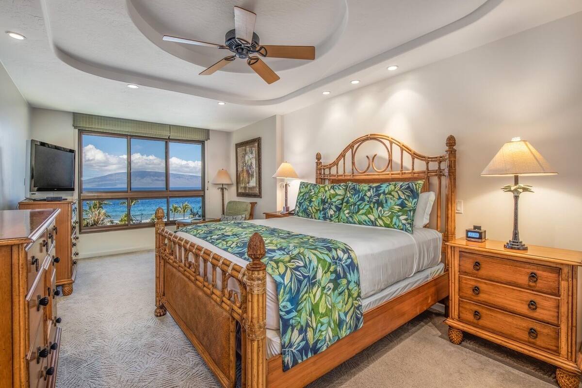 A bedroom with a bed, a television, a desk, and a view of the ocean.