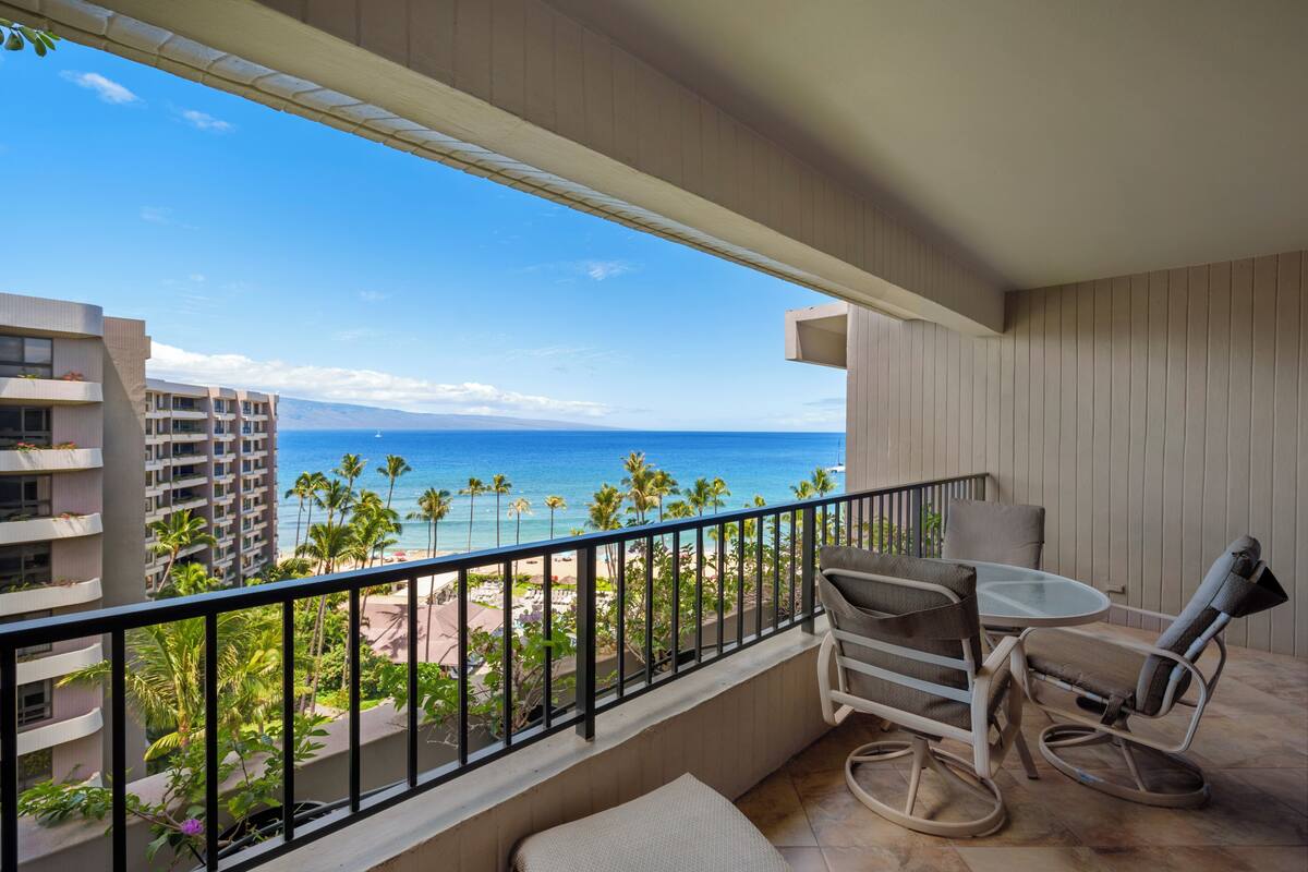 A balcony with a view of the ocean, a table with chairs, and a small seating area.
