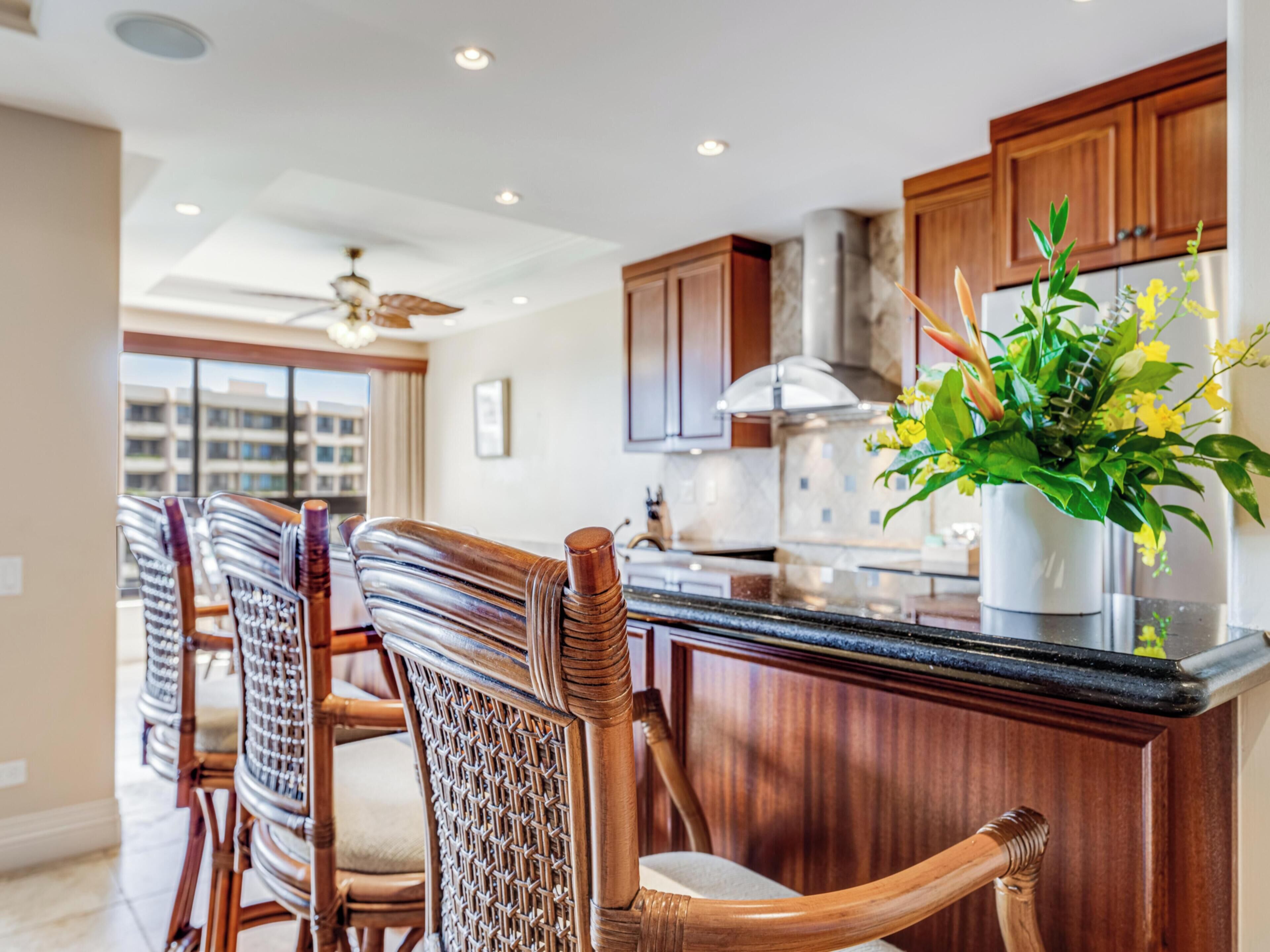 A modern kitchen with wooden cabinets, a black countertop, and a dining area with wicker chairs.