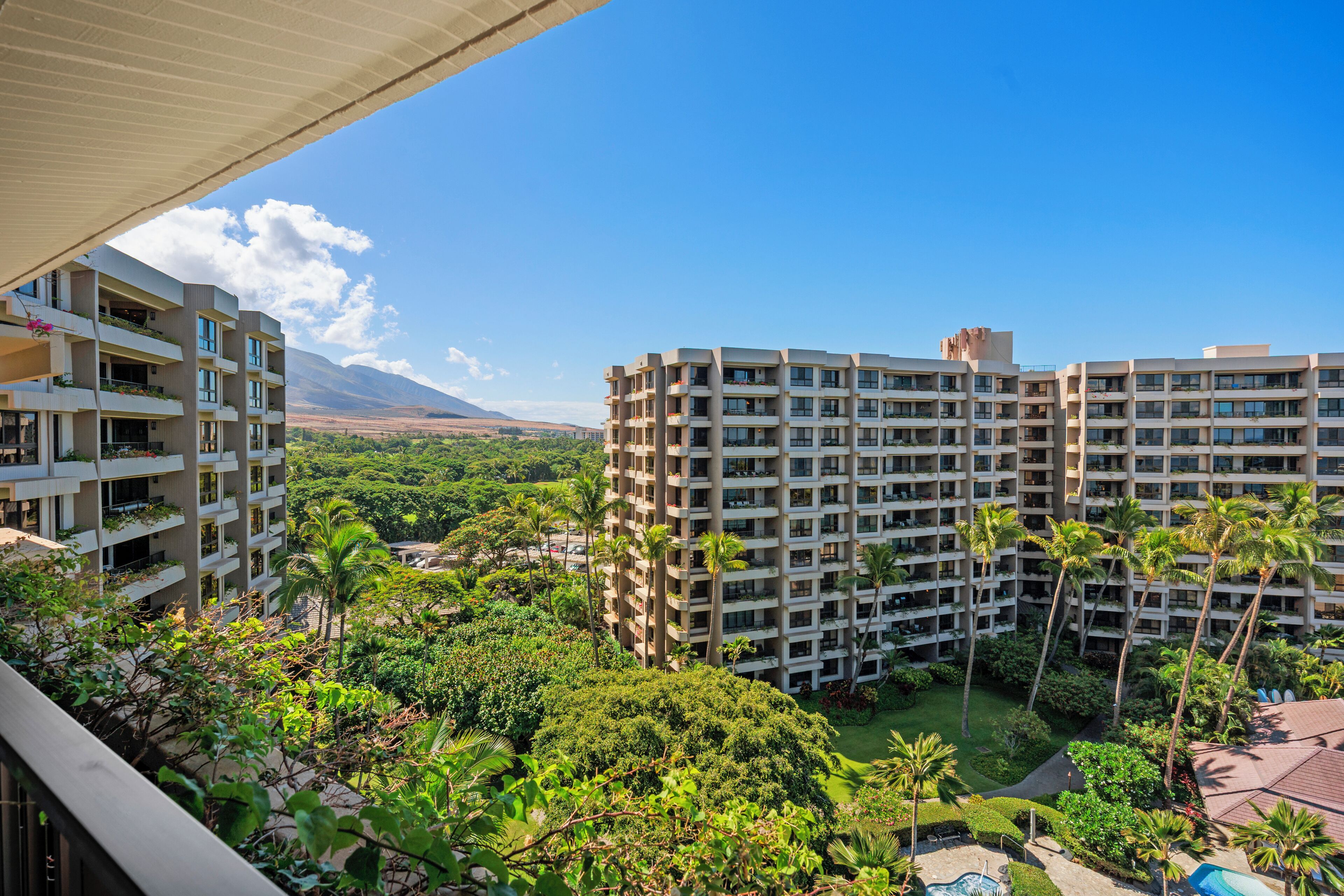 A high-rise hotel with multiple balconies, lush greenery, and a clear view of distant mountains.