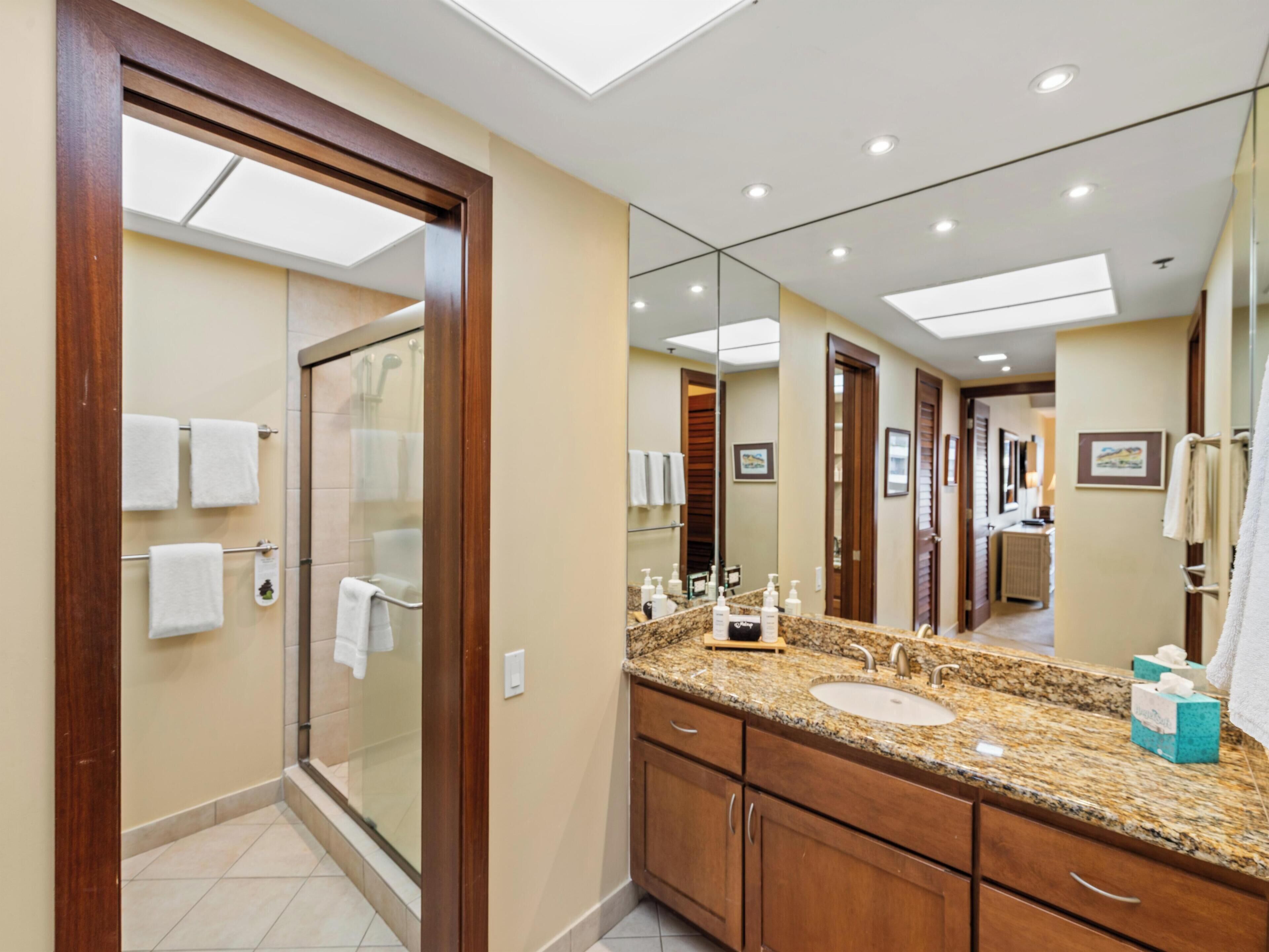 Un baño moderno con cabina de ducha de vidrio, tocador con encimera de granito y un espejo grande.