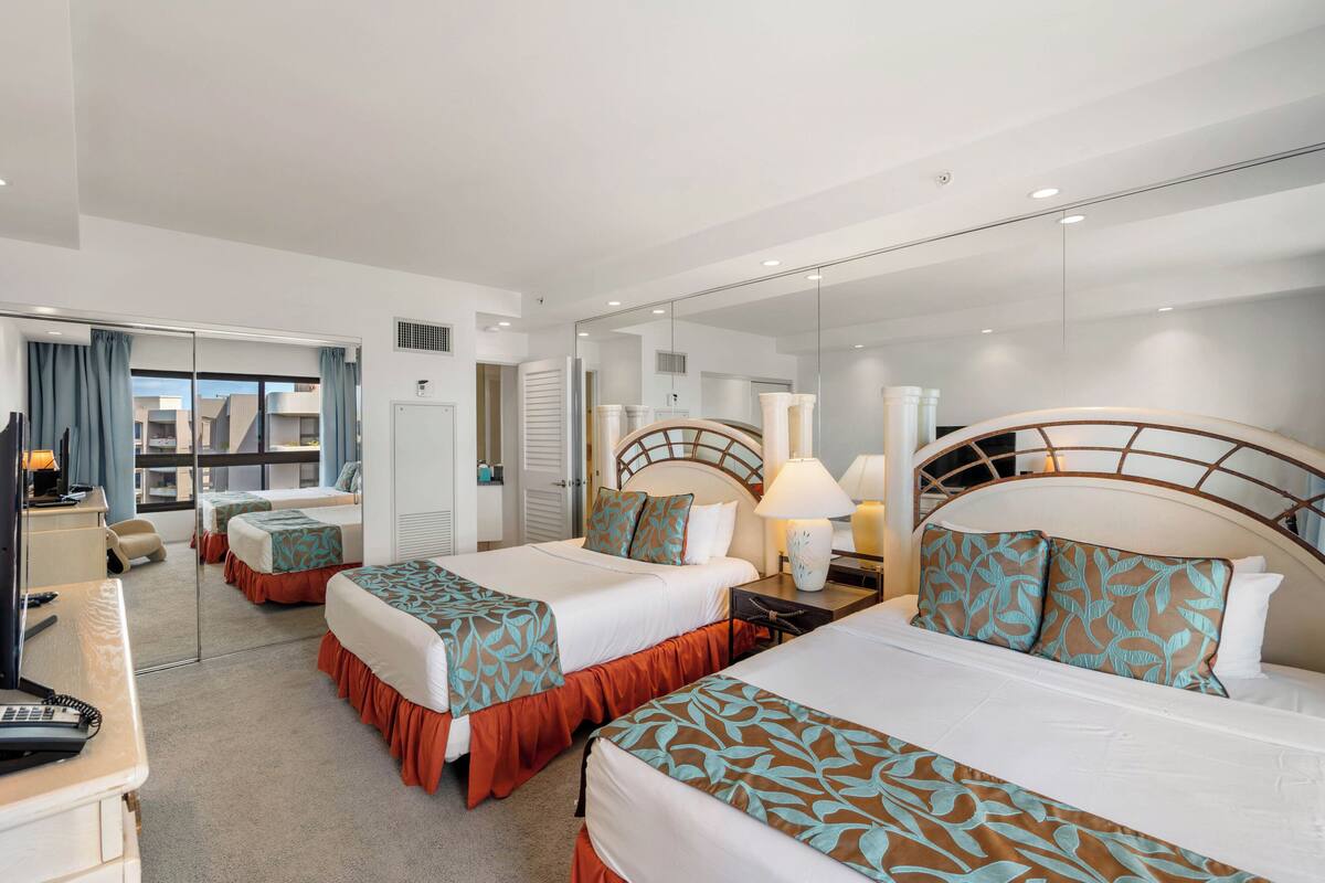 A hotel room with two beds, a desk with a computer, a mirror, and a view of the outside.