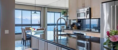 Een moderne keuken met een groot eiland, roestvrijstalen apparatuur en uitzicht op zee.