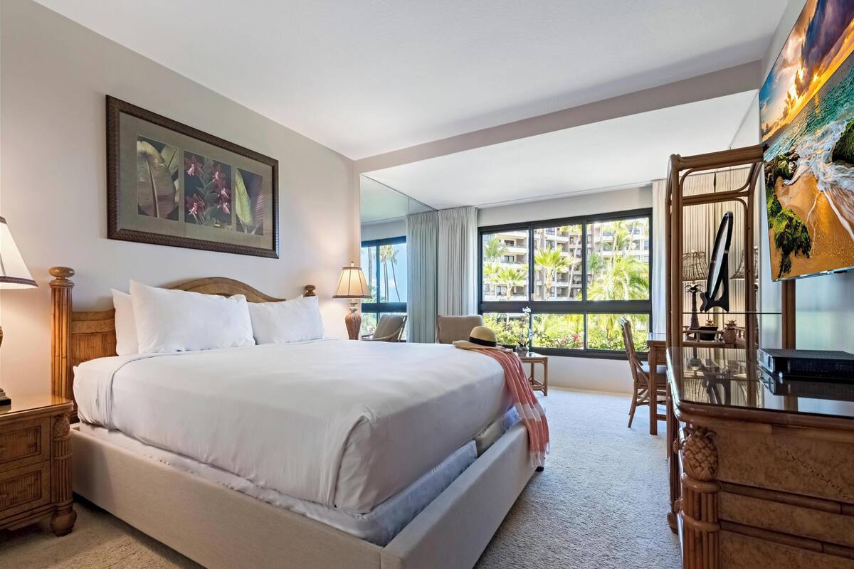A hotel room with a large bed, a desk, a chair, a lamp, and a painting on the wall.