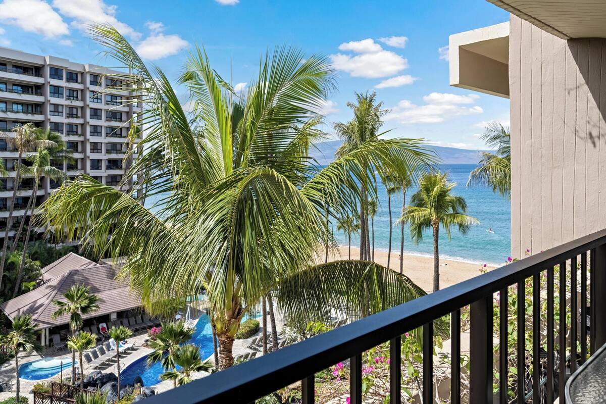 A hotel with a pool, palm trees, and a view of the beach and ocean.