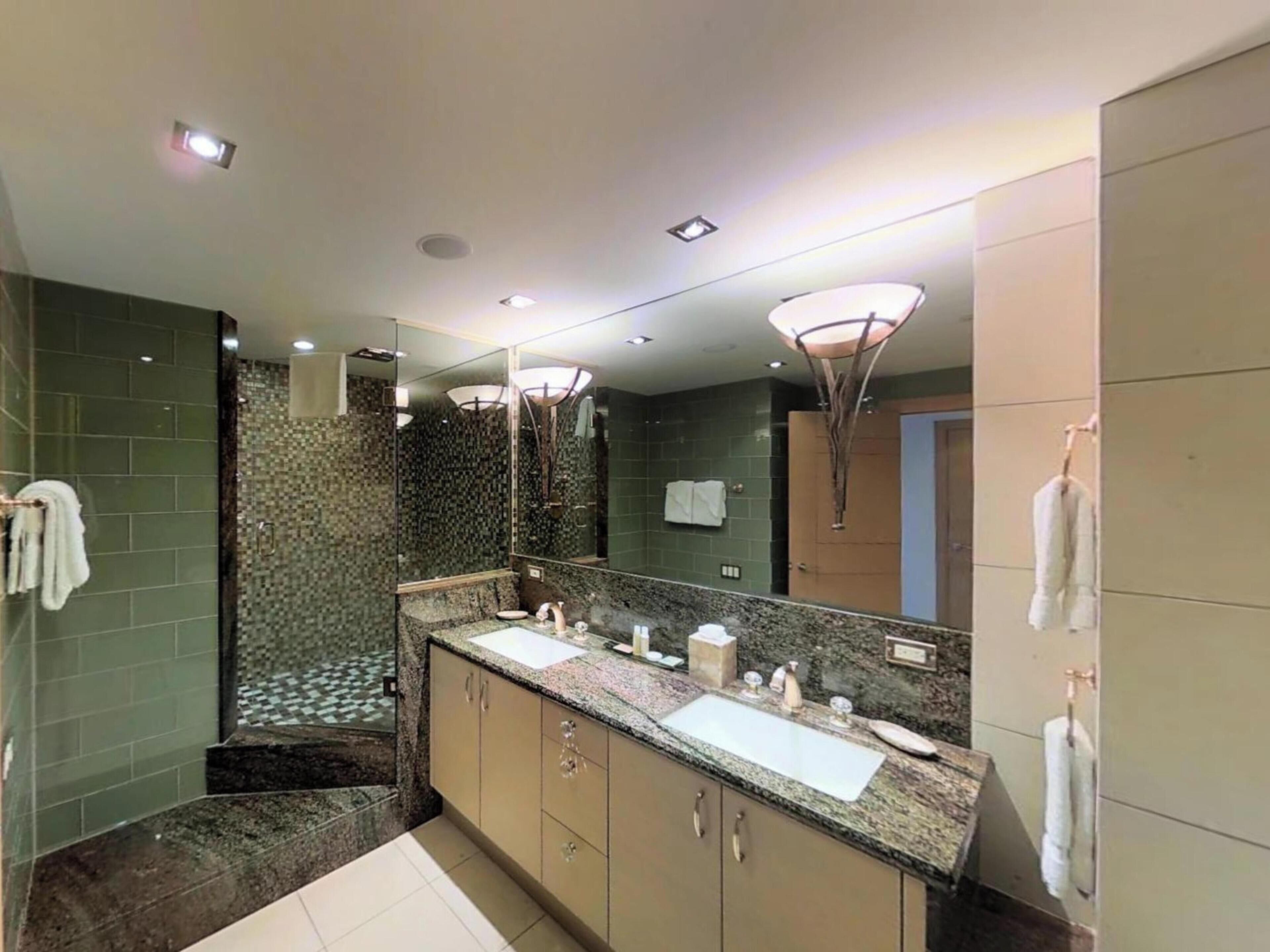 Un baño moderno con un espejo grande, dos lavamanos, una ducha y un perchero para toallas.