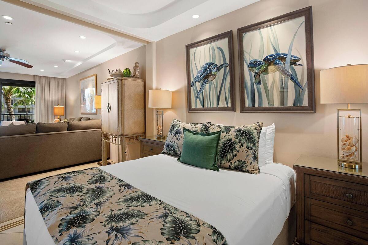 A hotel room with a bed, a sofa, a desk, and two framed paintings of sea turtles.