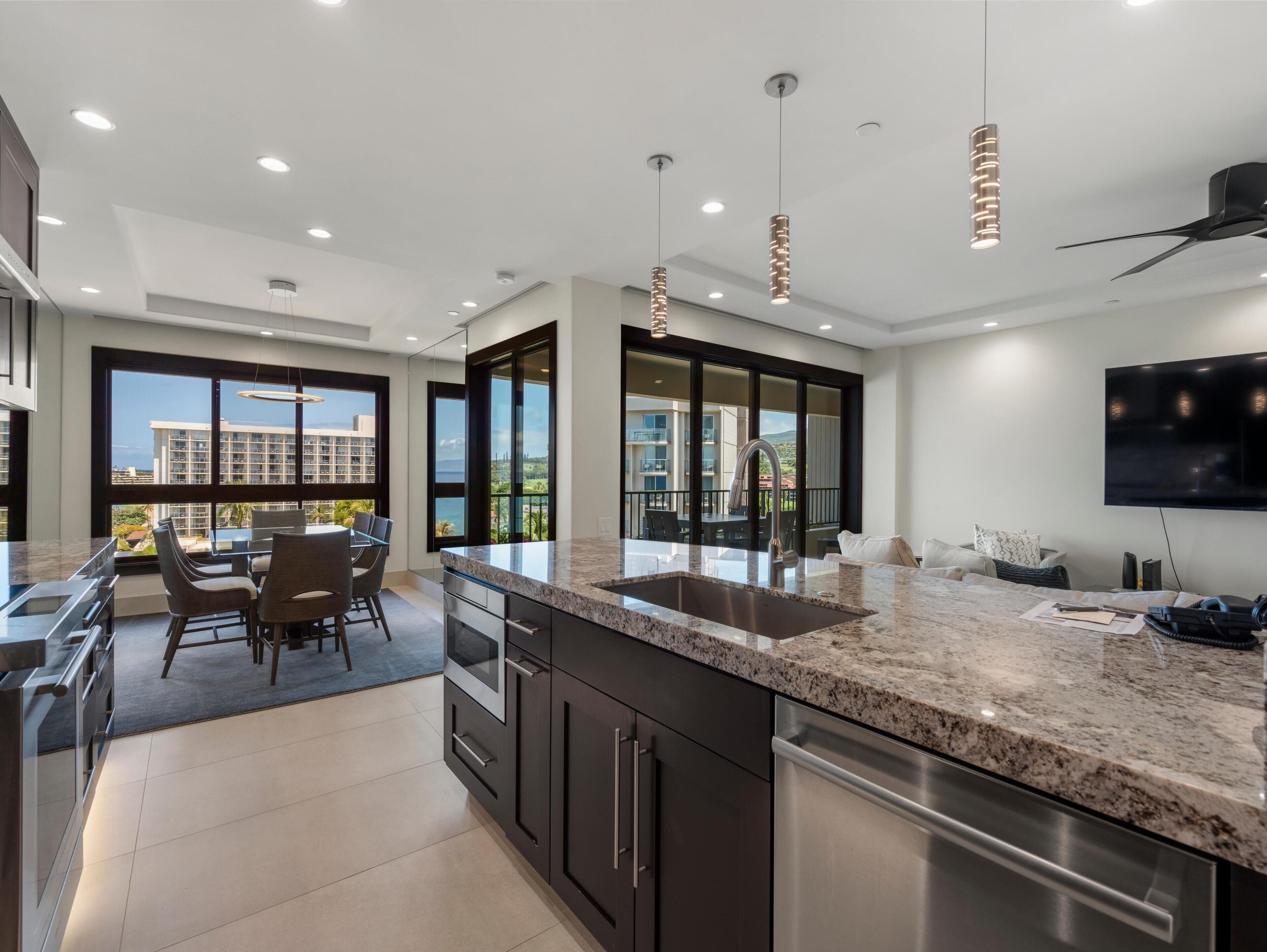 A modern kitchen with granite countertops, stainless steel appliances, and large windows offering a view of a cityscape.