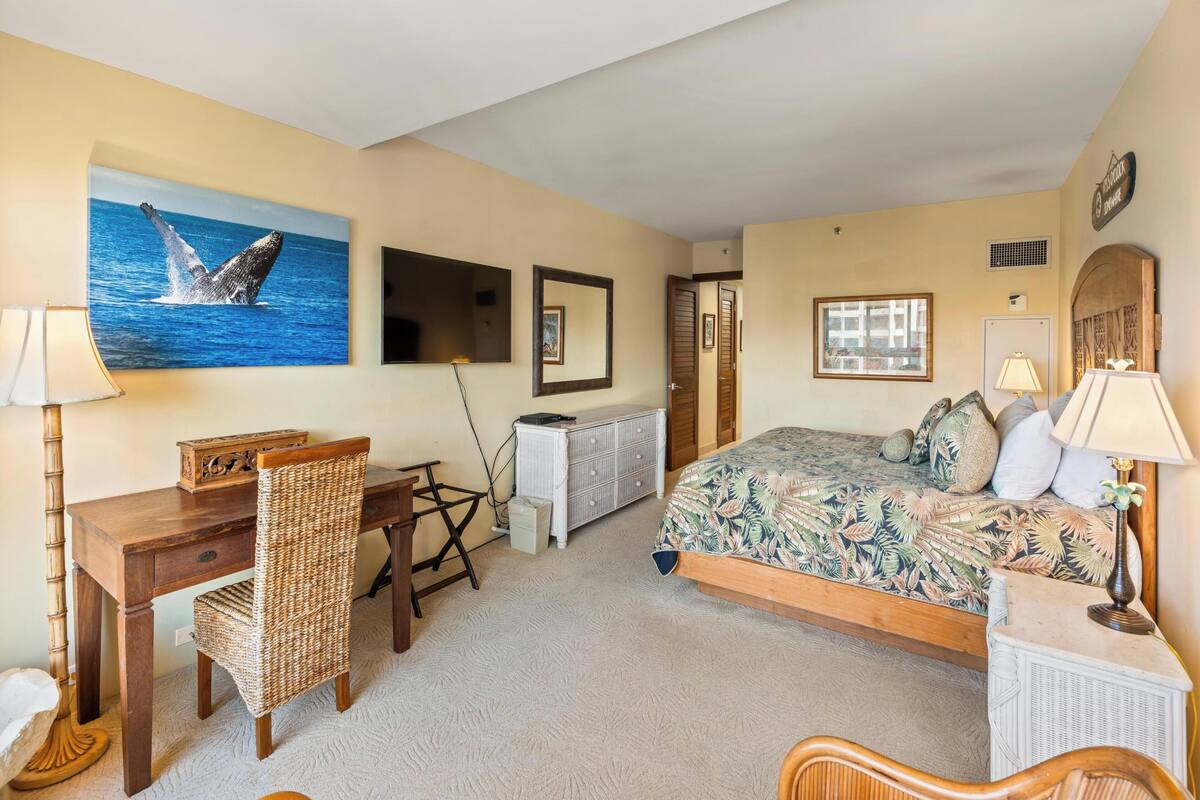 A bedroom with a bed, desk, chair, and a large painting of a whale.