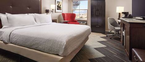 A hotel room with a large bed, a desk, a red chair, a TV, and a wardrobe.