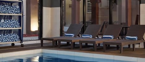 Un área junto a la piscina con sillones de descanso y una estantería con toallas.