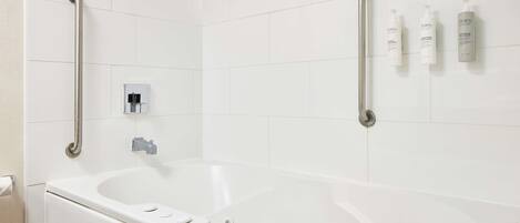 Une salle de bain moderne avec une baignoire blanche, des barres d’appui et des articles de toilette fixés au mur.