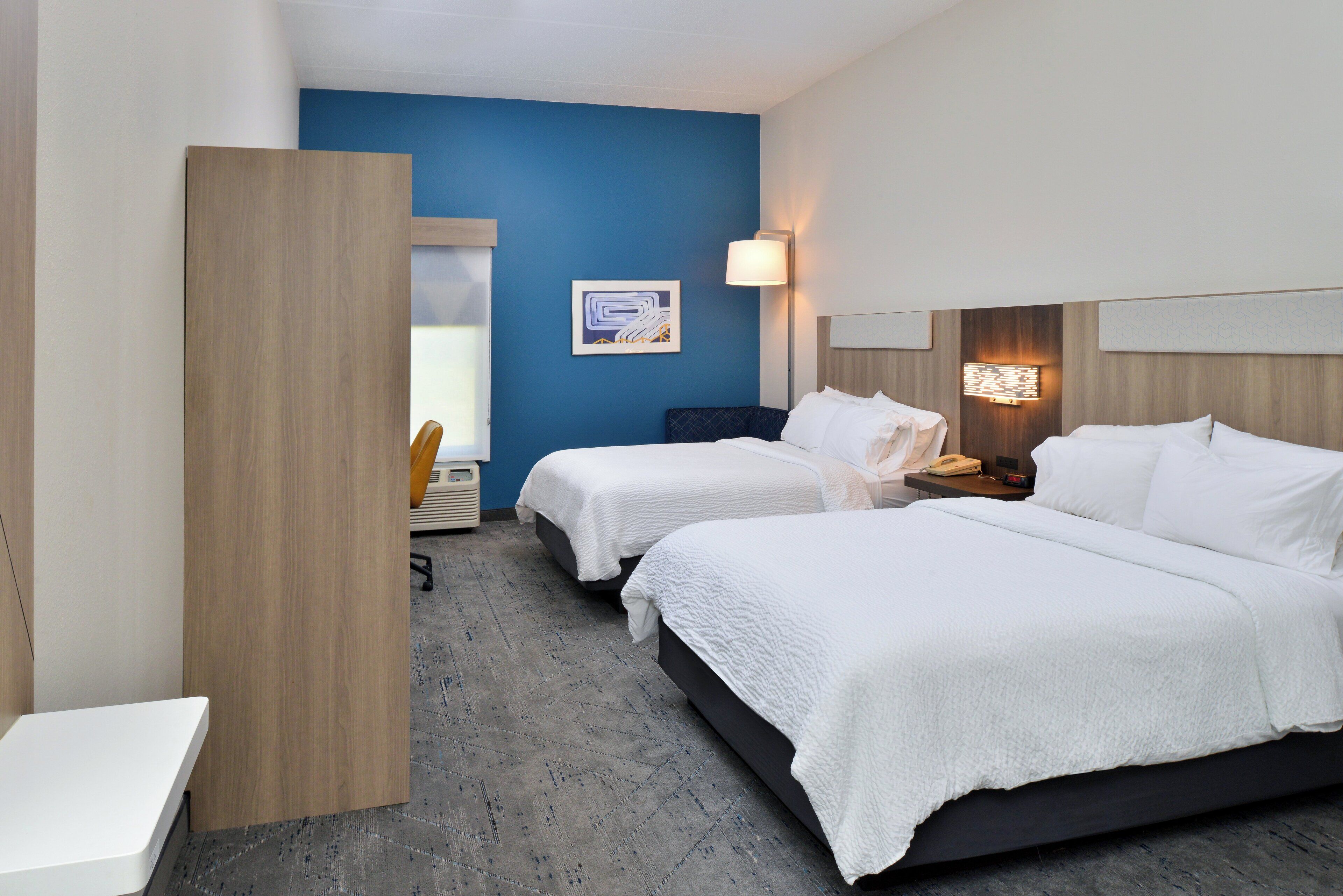 Habitación de hotel con dos camas, un escritorio, una silla y una ventana.