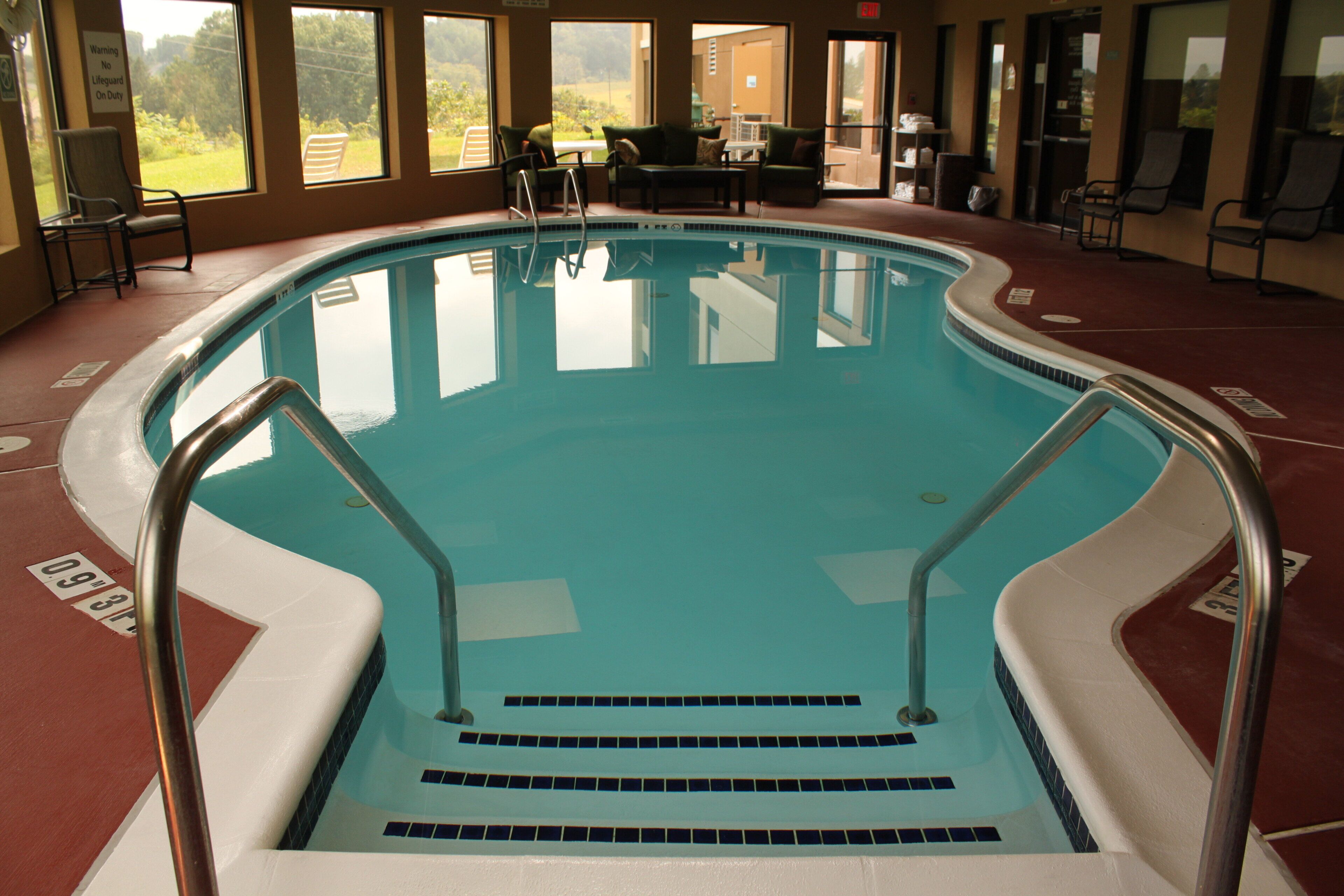 An indoor swimming pool with steps leading into the water, surrounded by chairs and tables.