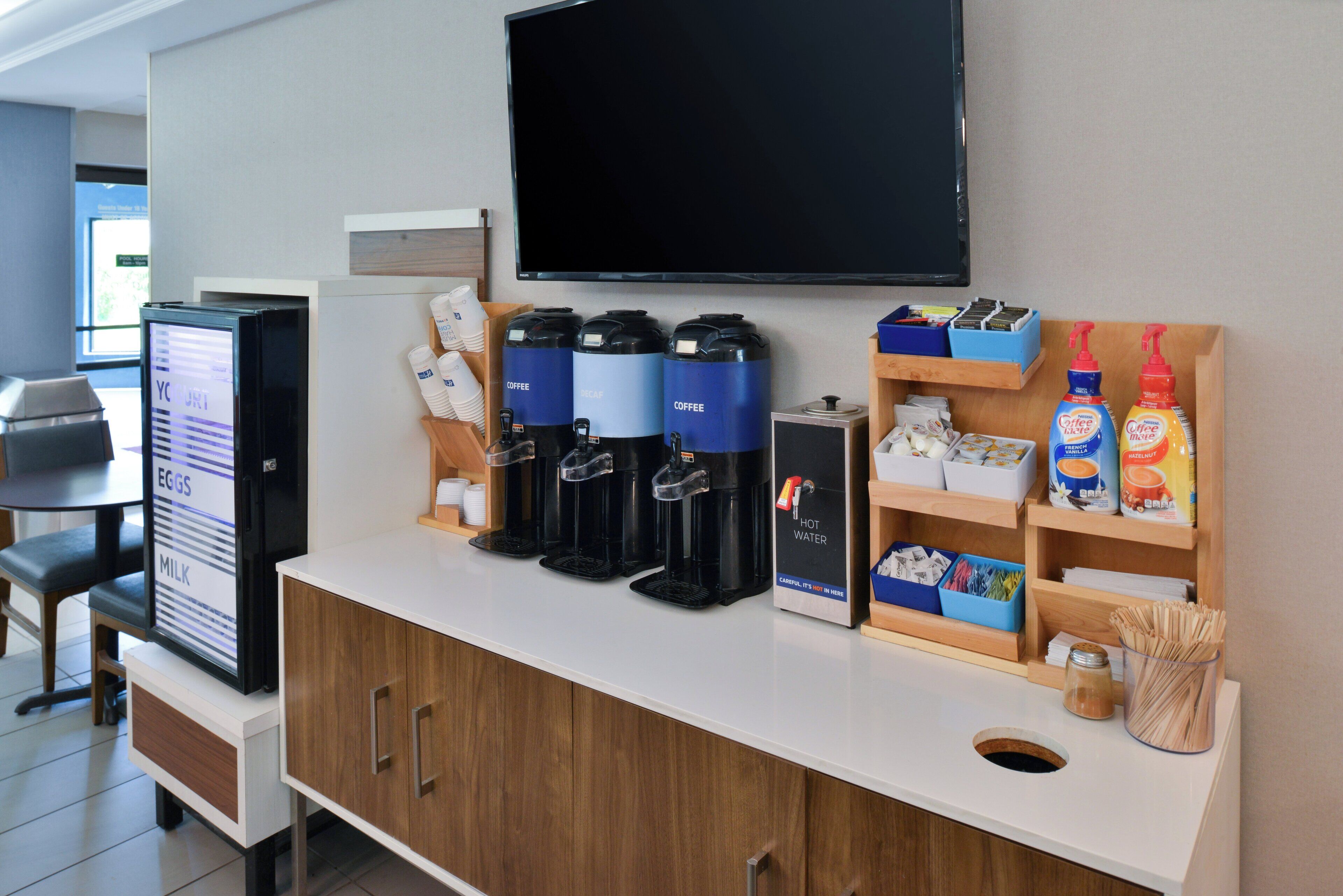 A hotel reception area with a coffee machine, a television, and various amenities including a menu board and toiletries.