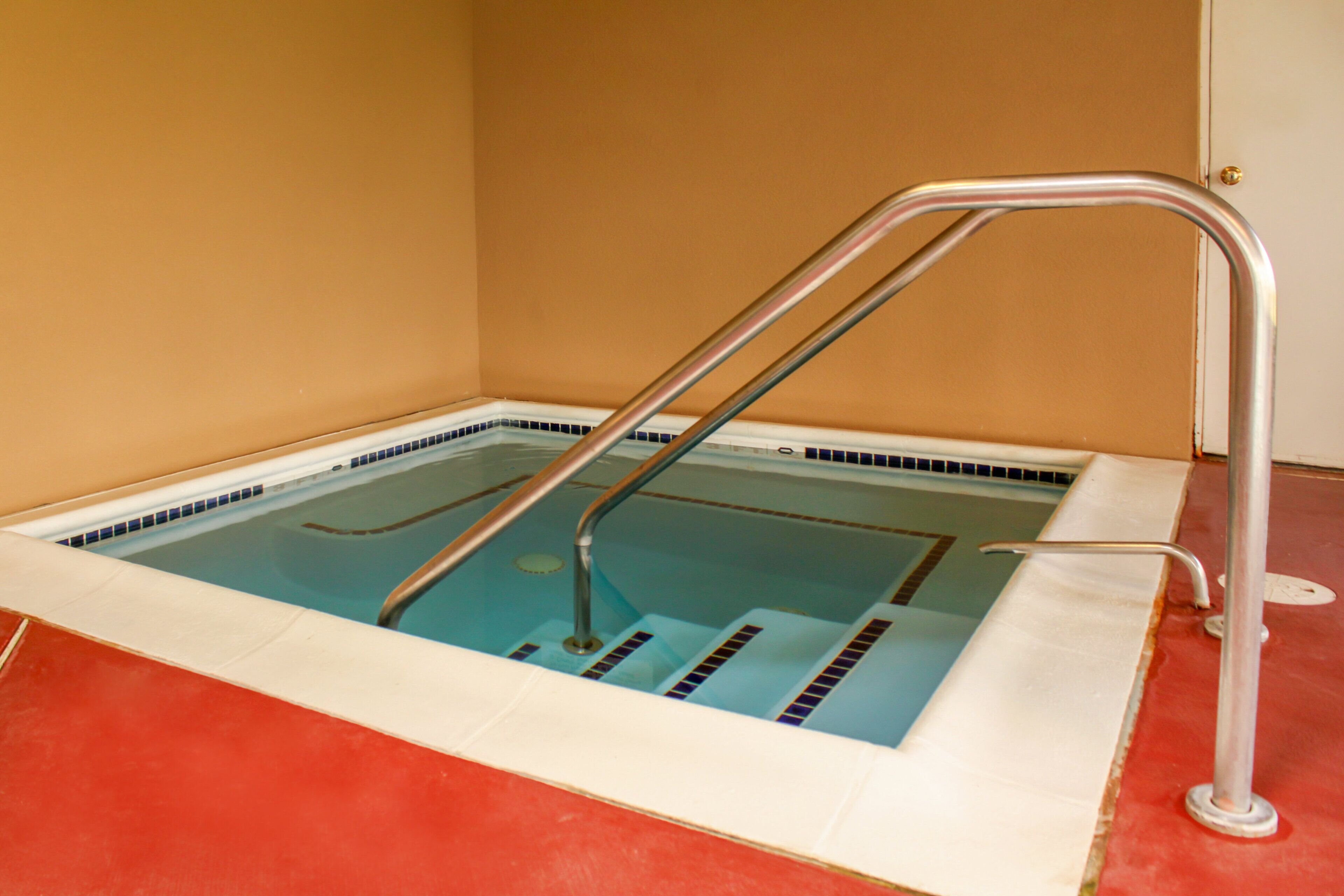 Una pequeña piscina interior con una escalera metálica y suelo rojo.