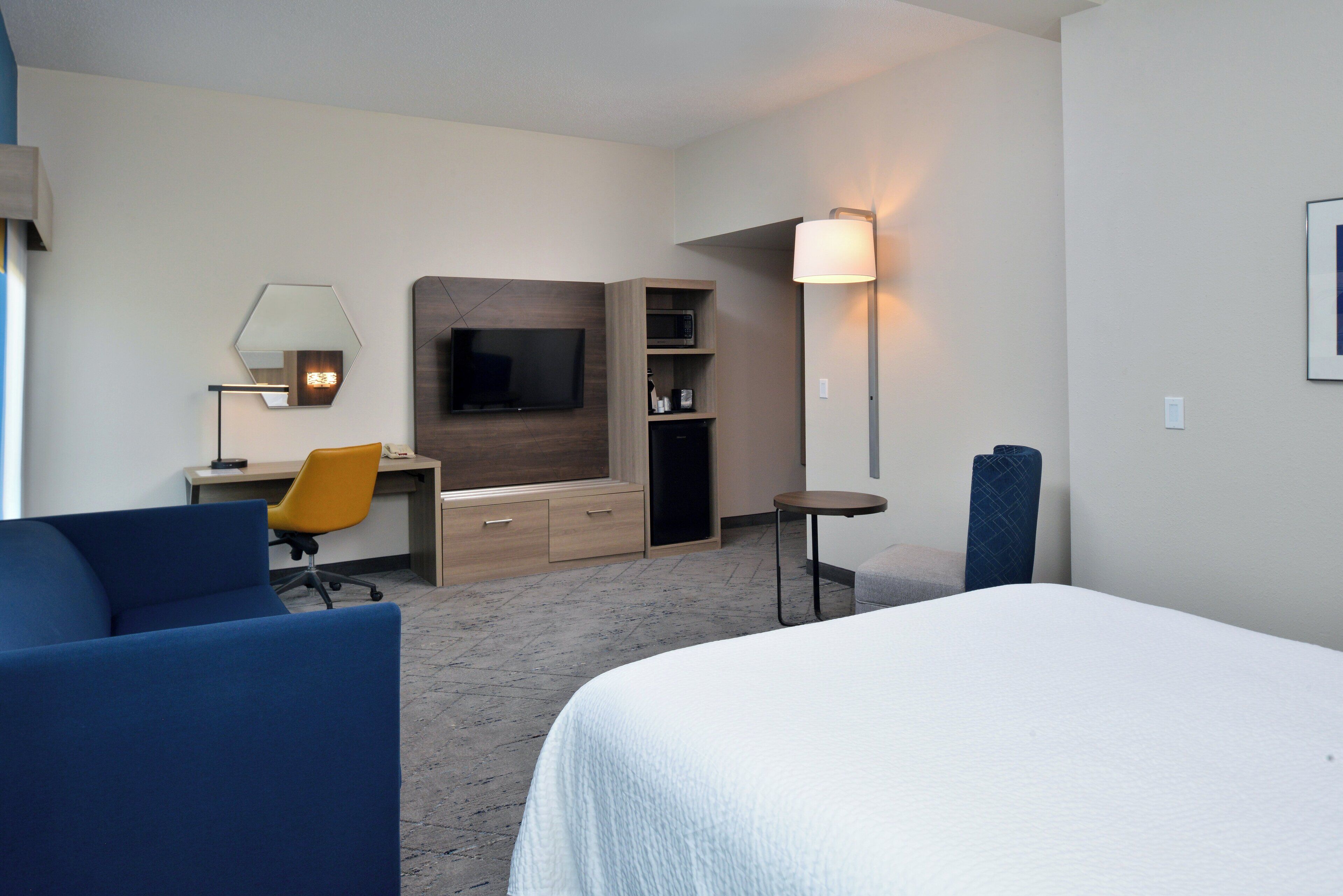 Une chambre d’hôtel équipée d’un lit, d’un bureau avec une chaise, d’une télévision, d’une lampe et d’un four à micro-ondes.