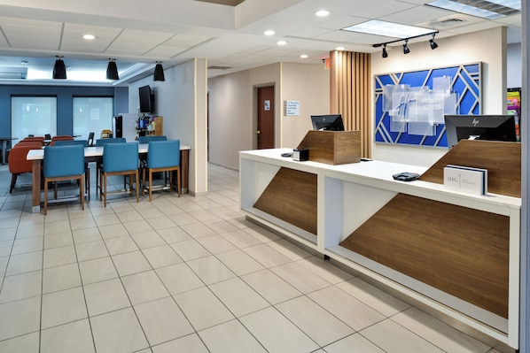 A hotel reception area with a modern design, featuring a reception desk, seating area with tables and chairs, and a large blue and white geometric wall decoration. - Holiday Inn Express Lewisburg/New Columbia by IHG (New Columbia)
