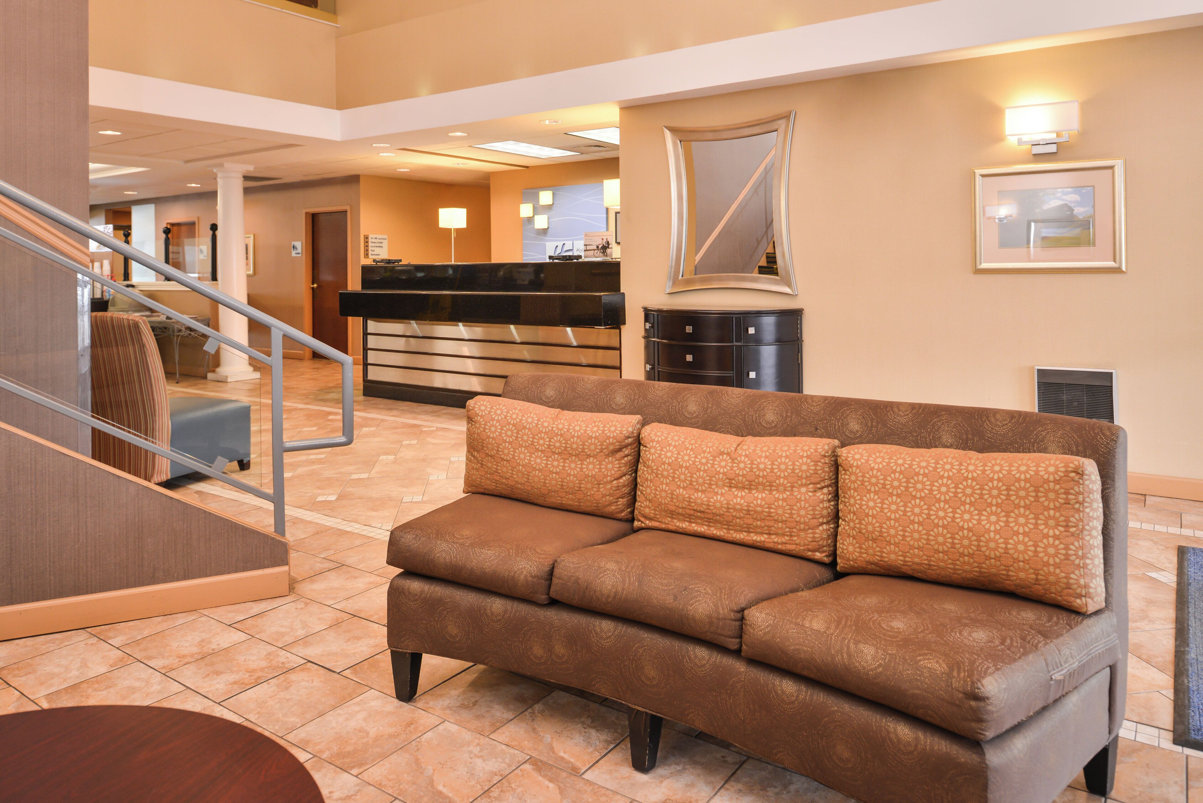 En hotelllobby med en brun soffa, en receptionsdisk och en trappa.