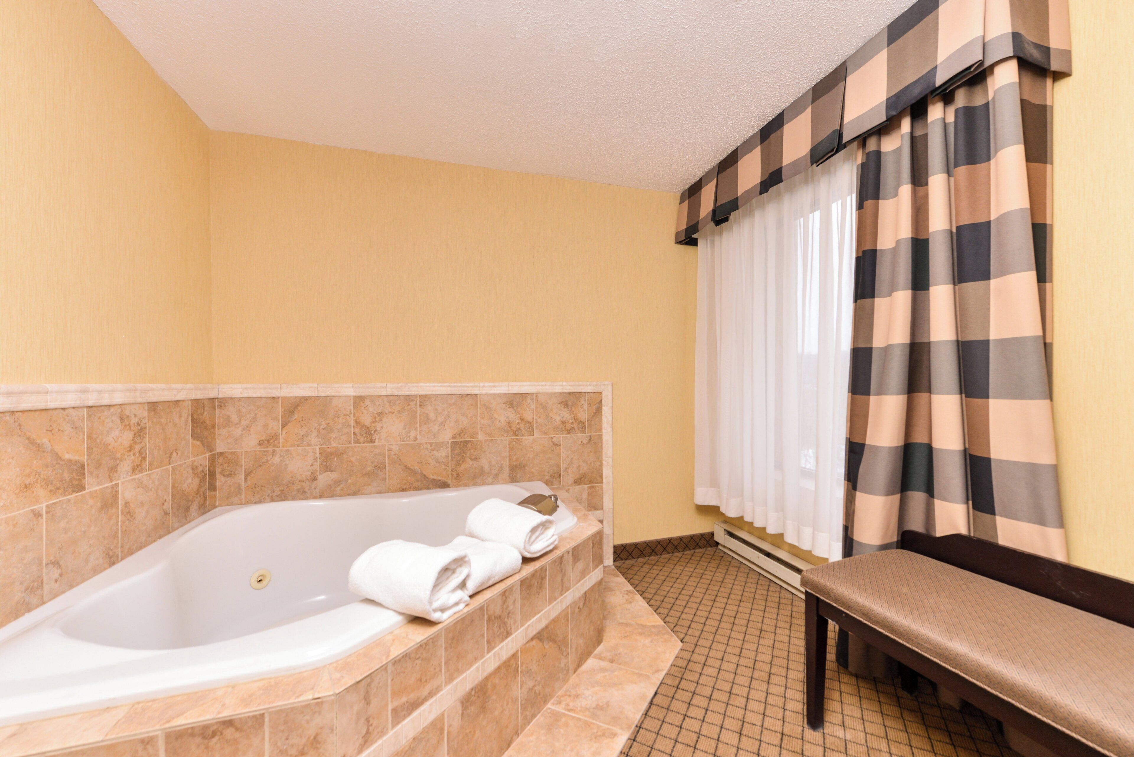 Un baño con una bañera, un banco y una cortina a cuadros.