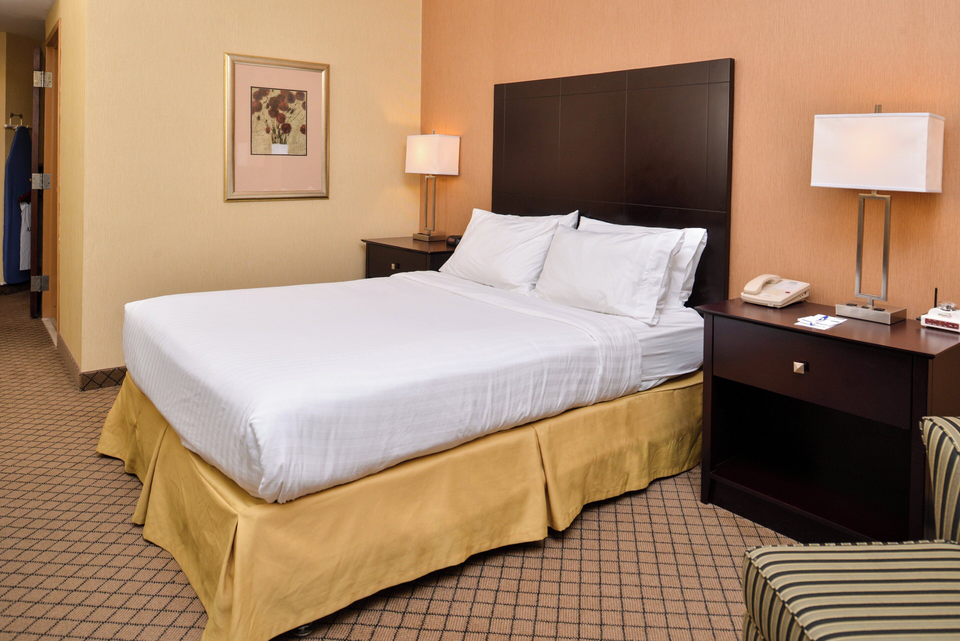 A hotel room with a large bed, two bedside tables, a nightstand, a chair, and a wall-mounted telephone.